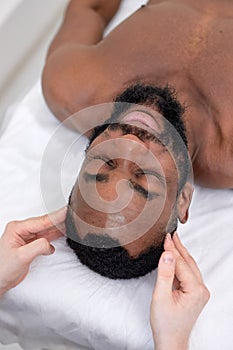Spa therapist making relaxing massage for handsome middle aged black man, top view
