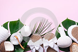 Spa tools: white towel, bamboo slippers, herbal ball, cream, wooden brush, coconut oil, monstera on pink background. Cosmetic