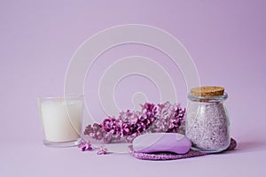 Spa treatment with natural soap, body care sea salt, lilac flowers and candle on purple background