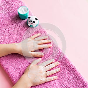 Spa treatments for hand skin and nails for children. Young girl`s hands lie on pink soft towel smeared with white cream.
