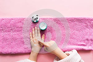 Spa treatments for hand skin and nails for children. Young girl`s hands lie on pink soft towel smeared with white cream.