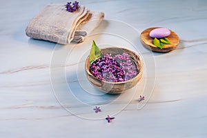 Spa and wellness composition with perfumed lilac flowers water in wooden bowl.