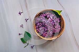 Spa and wellness composition with perfumed lilac flowers water in wooden bowl on marble background.