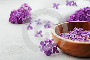 Spa and wellness composition with perfumed lilac flowers water in wooden bowl and terry towel on stone background, aromatherapy
