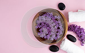 Spa and wellness concept with lilac flowers in water in a wooden bowl and towel aromatherapy and black stones, top view, flat lay