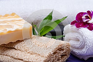 Spa Wellness Concept. Natural Loofah Sponge, Almond Goat`s milk Soap, White Towels, Basalt Stones, Bamboo and Orchid Flower