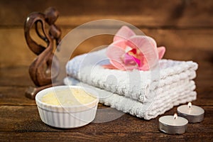 Spa or wellness set. Yellow sea salt in white bowl, candle, towels, brown wooden statuette and pink flowers lily on brown wooden