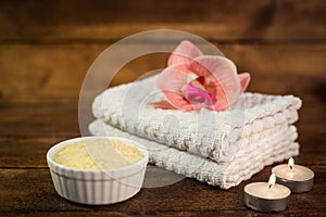 Spa or wellness set. Yellow sea salt in white bowl, towels, candle and pink flowers lily on brown wooden background. Selective