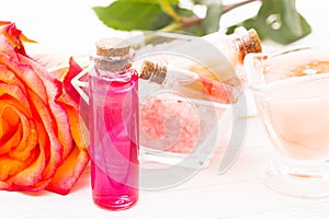 Spa and wellness setting with rose flower, sea salt, oil in a bottle on wooden white background