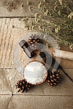 Spa and wellness setting with sea salt, oil essence, cones and candle on wooden background. Fall autumn wellness concept, Relax