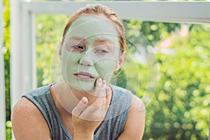 Spa Woman applying Facial green clay Mask. Beauty Treatments. Close-up portrait of beautiful girl applying facial mask