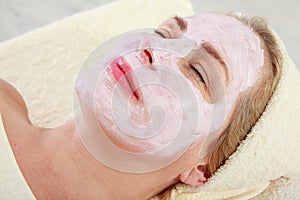 Spa Woman applying Facial Mask. Beauty Treatments. Close-up portrait of beautiful middle-aged woman with a towel on her