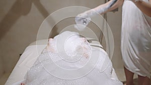 Spa worker washes woman under bubble soap foam with a stream of water in hammam shower. Female relax, gets body skin