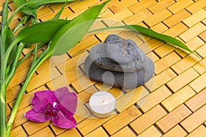 Spa, zen, massage concept. Bamboo leaves, black stones, purple orchid, candle on wood background