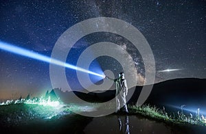 Space traveler shining flashlight into beautiful starry sky.