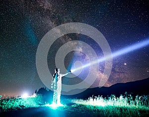 Space traveler shining flashlight into majestic night sky.