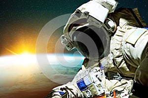 Spaceman in a space suit with a helmet on the background of the planet earth with amazing yellow rays of the sun. Astronaut in