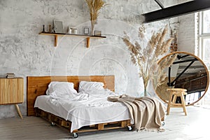 Spacious airy white eco style loft bedroom with bed,  mirror and pampas grass decoration