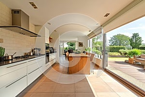 Spacious bright kitchen interior in a modern luxury villa. White cabinets, built-in home appliances, dining area, large