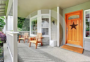 Spacious concrete porch with wooden chairs and nice entry door.