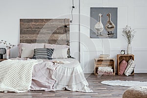 Spacious, feminine bedroom interior with rustic furniture, white walls, wooden crates and oil painting of animals. Real photo