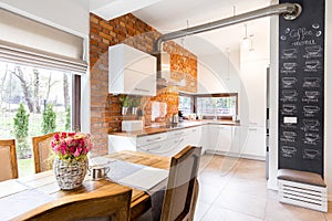 Spacious kitchen with white furniture and brick wall
