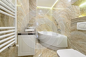 Luxury bathroom with white bathub and beige marble tiles