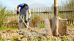 Spade sticking into the earth with a woman working on the background