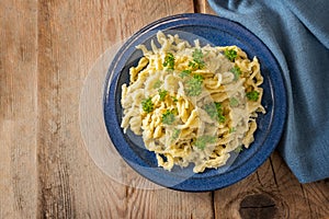 Spaetzle, homemade egg noodles served with parsley garnish on a blue plate and a rustic wooden table with copy space, traditional