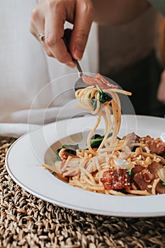 Spaghetti bacon, garlic, basil, dried chili pepper on fork on wood table.