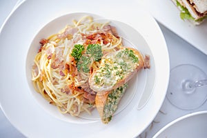 Spaghetti with bacon and garlic bread on white dish