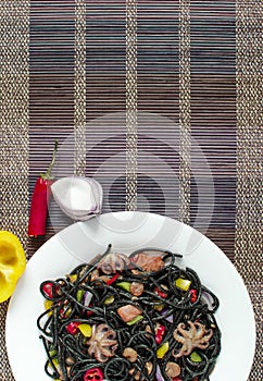 Spaghetti black with seafood and vegetables on a white plate multi-colored background top view vertical