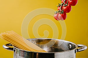 spaghetti boiling in stewpot with branch of cherry tomatoes above isolated on yellow