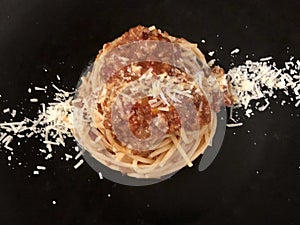 Spaghetti Bolognese with cheese . Black background .