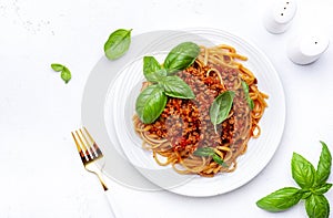 Spaghetti bolognese or pasta with minced meat in tomato sauce with green basil, white table background, top view