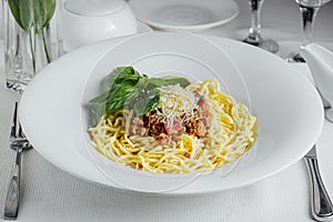 Spaghetti bolognese on a white plate with wide fields on a serving table
