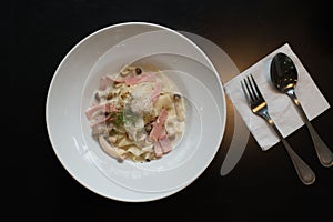 Spaghetti cream sauce ham and mushroom serve on white dish.