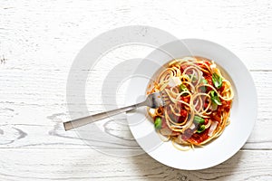 Spaghetti with fork, tomato sauce, fresh basil and cheese. Isolated on white wood from above.