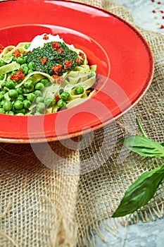 Spaghetti with fresh green peas. Gray textured background with beige fabric. Beautiful serving of dishes. Restaurant