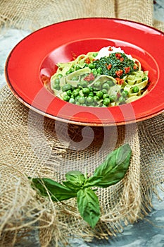 Spaghetti with fresh green peas. Gray textured background with beige fabric. Beautiful serving of dishes. Restaurant