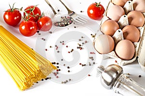 Spaghetti lie on a white background, along with cherry tomatoes, a spoon and a fork