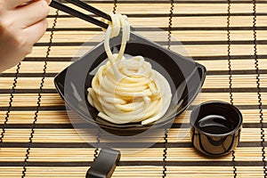 Spaghetti macaroni in black ceramic plate with chopsticks at striped bamboo mat