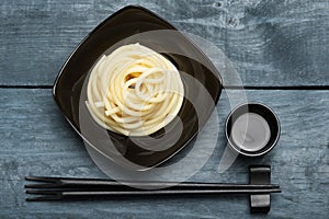 Spaghetti macaroni in black plate with chopsticks at wooden table