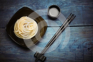 Spaghetti macaroni in black plate with chopsticks at wooden table