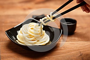 Spaghetti macaroni in black plate with chopsticks at wooden table