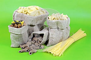 Spaghetti and Macaroni of Different Shapes and Colors in Jute Bag on Green