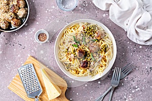 Spaghetti with meatballs and cream sauce is served on a plate with herbs and parmesan.