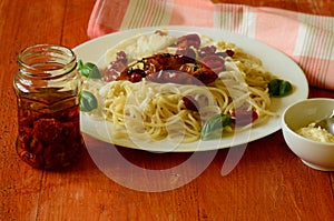 Spaghetti with mozzarella, dried tomatoes and basil on red background