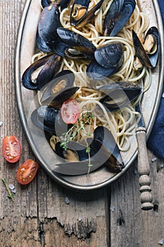 Spaghetti with mussels, tomatoes in spicy sauce in the original plate on the old wooden table. Clams Mytilus closeup.