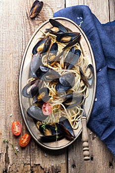 Spaghetti with mussels, tomatoes in spicy sauce in the original plate on the old wooden table. Clams Mytilus closeup.